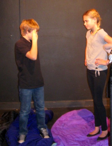 Two actors facing each other, one hands on hips, the other fingers pressed to temple