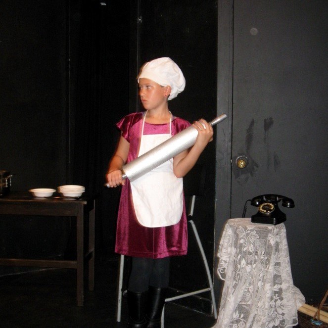 An actor dressed as a cook holding a giant rolling pin