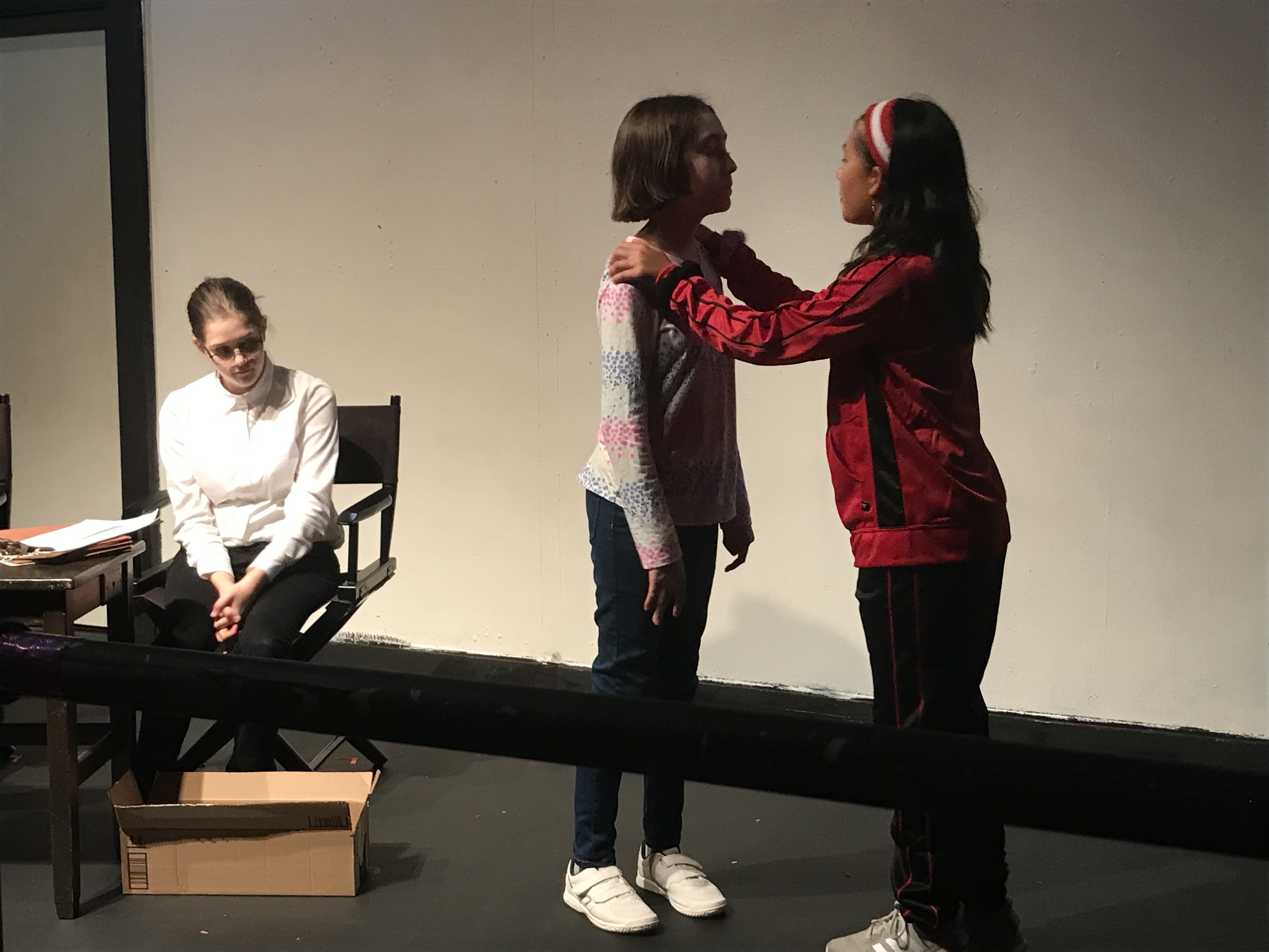 Two actors facing each other while another actor sits off to the left