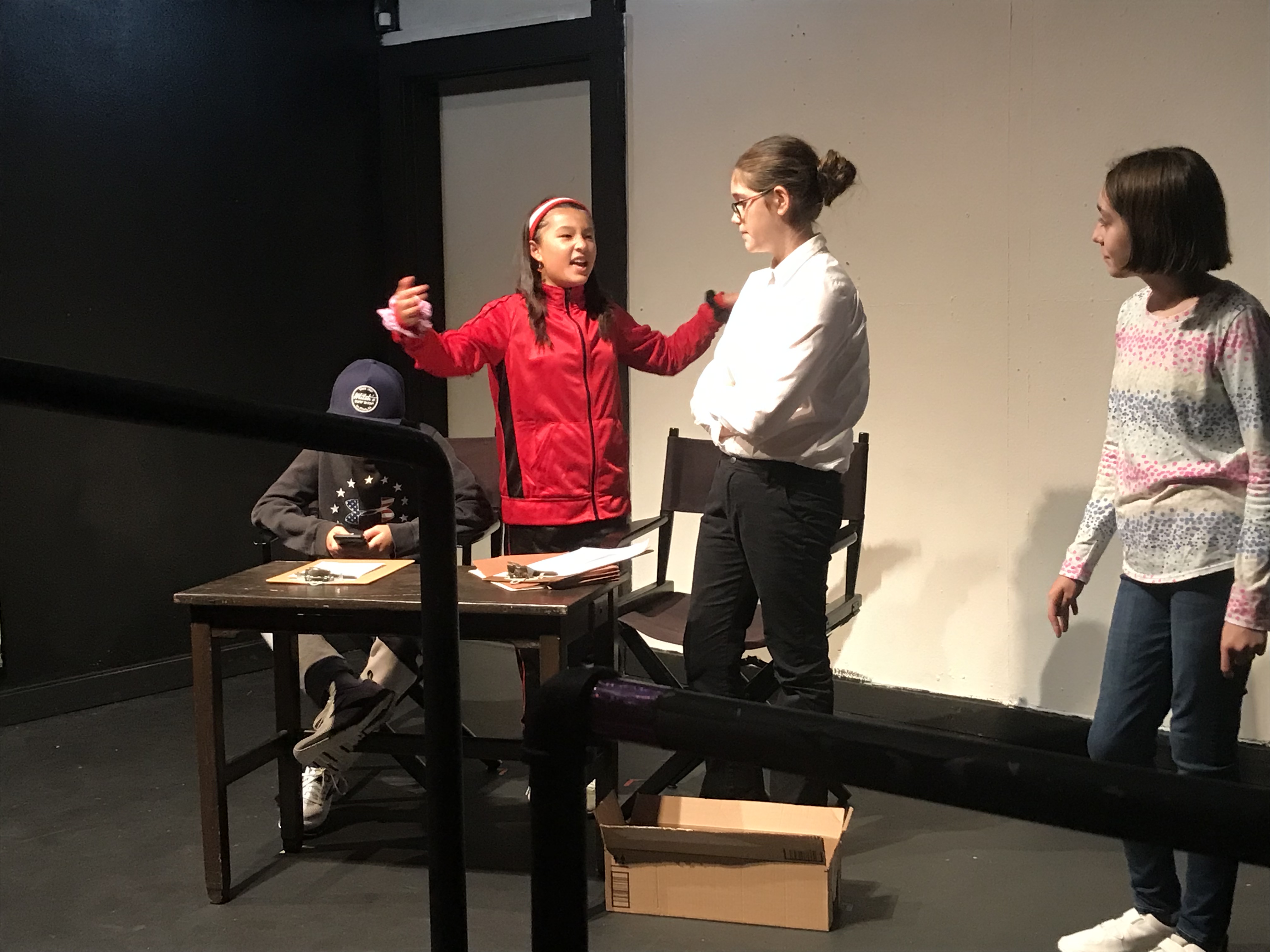 Four actors onstage, one in the middle has hands up and looks crazy